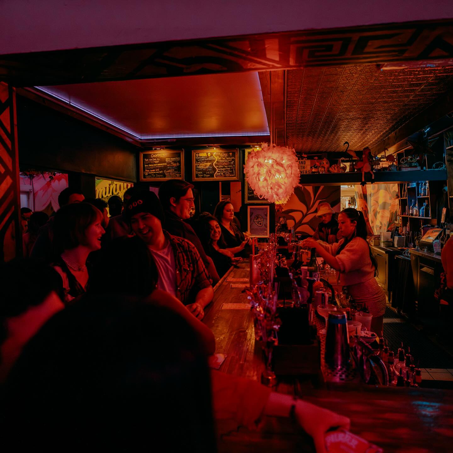 Bartender pouring cocktails for a lively crowd at Flamingo House bar under warm red lighting in Midtown Sacramento